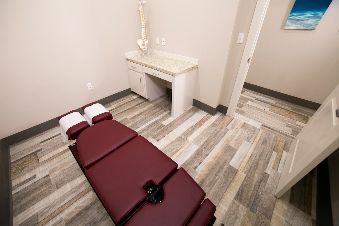 Chiropractic exam room with burgundy adjustment table and spine model.